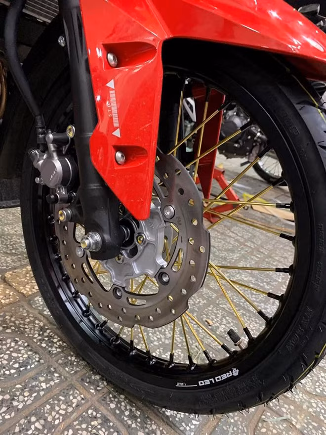 Dàn chân nguyên bản trên côn tay Honda Winner X được thay thế bằng cặp vành nhôm đến từ thương hiệu Red Leo kết hợp cùng bộ căm vàng nổi bật. Bánh căm mới này có kích thước 1.4 ở phía trước và 1.6 ở phía sau, cặp lốp nguyên bản cũng đã được chủ nhân thay bằng lốp đến từ hãng Quick và Maxis. Sử dụng bánh căm giúp cho xe vượt qua các địa hình êm ái hơn, ngoài ra khối lượng xe cũng được giảm đáng kể.