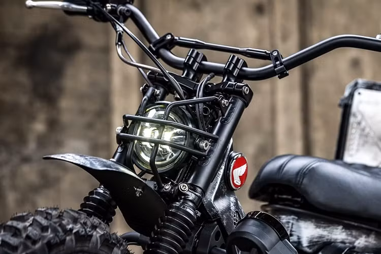 Có thể thấy, bản độ CT125 Combat đã mang lại vẻ ngoài hoàn toàn mới mẻ so với chiếc Honda CT125 nguyên bản. Ở dàn đầu xe thì đèn pha đã được thay thế bằng một đèn độ nhỏ gọn hơn, đi kèm với đó là lưới bảo vệ bằng kim loại dày dặn ở phía trước.