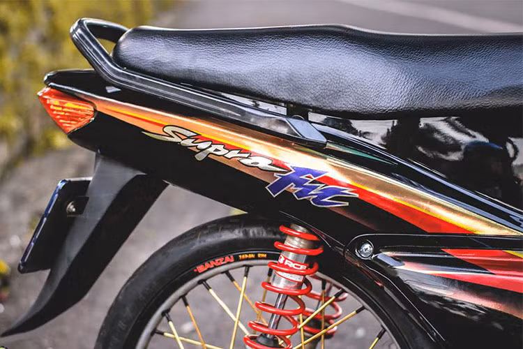 Giảm xóc sau Racing boy cho độ nhún êm ái hơn cũng như tăng độ cứng cáp cho xe với lò xo màu đỏ nổi bật cùng với lốp mới bánh căm. Cỗ máy 110cc trên chiếc xe máy Honda Wave cũ này vẫn được giữ nguyên bản, chỉ dọn lại và trang trí thêm một số chi tiết ơpr ốp ngoài.