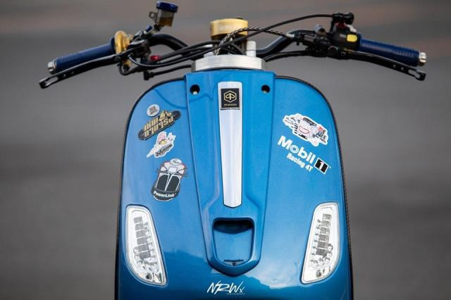 Đầu đèn của mẫu xe tay ga Vespa LX đã được tháo bỏ, thay vào đó là cụm ghi đông trần với trợ lực trung tâm Scott. Phần yếm trước vẫn giữ nguyên nhưng được chủ nhân dán thêm các hình dáng tạo điểm nhấn và nét riêng.
