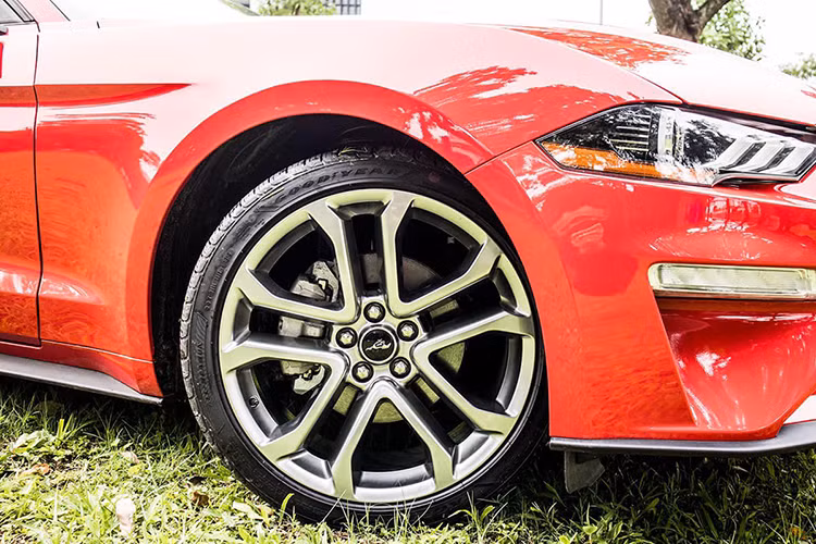 Ford Mustang kỷ niệm 55 năm ra đời là bản Premium nên xe sử dụng bộ mâm hợp kim màu titan với kích thước đến 20 inch 5 chấu kép hình chữ “V”. Gương chiếu hậu của xe không tích hợp đèn xi-nhan nhưng có tính năng cảnh báo điểm mù. Đuôi xe nổi bật nhờ cụm đèn hậu với thiết kế 3 dải LED ấn tượng, cặp ống xả đôi xuất hiện kèm đèn phản quang kết hợp với hệ thống cản sau góc cạnh.