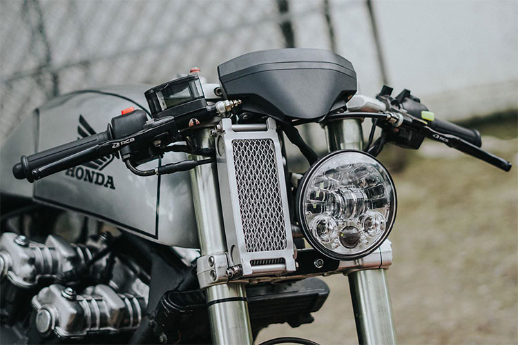 Về thiết kế của chiếc Honda CB750 độ cafe racer này, thay vì kiểu dáng đầu đèn tròn cổ điển, xưởng độ đã khiến chiếc xe cá tính hơn với phần đầu là một đèn LED dạng thấu kính projector hiện đại, bên cạnh đó là két tản nhiệt dầu được thiết kế đẩy hẳn lên cao sát với tay lái của chiếc xe. 