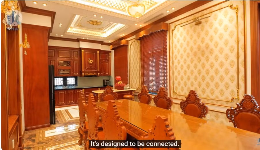 Phòng ăn và bếp liên thông với nhau. Bàn ăn lớn bằng gỗ gõ đỏ nguyên khối. Ảnh chụp màn hình NhaF