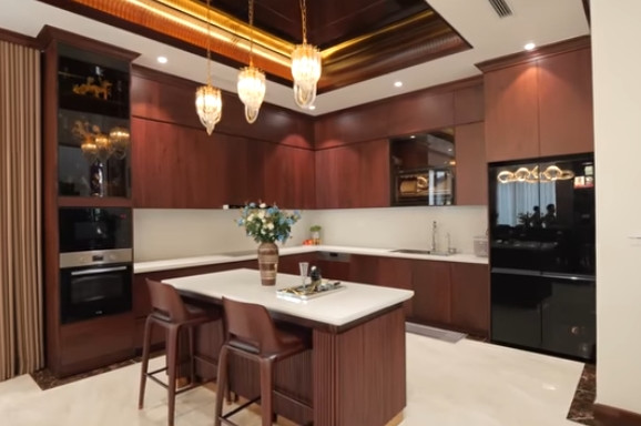 Bếp có bàn đảo bằng gỗ óc chó kết hợp mặt đá nhân tạo, phía trên là đèn trang trí. Ảnh chụp màn hình NhaF