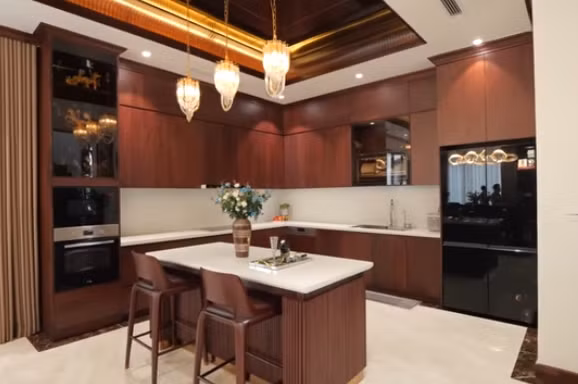 Bếp có bàn đảo bằng gỗ óc chó kết hợp mặt đá nhân tạo, phía trên là đèn trang trí. Ảnh chụp màn hình NhaF