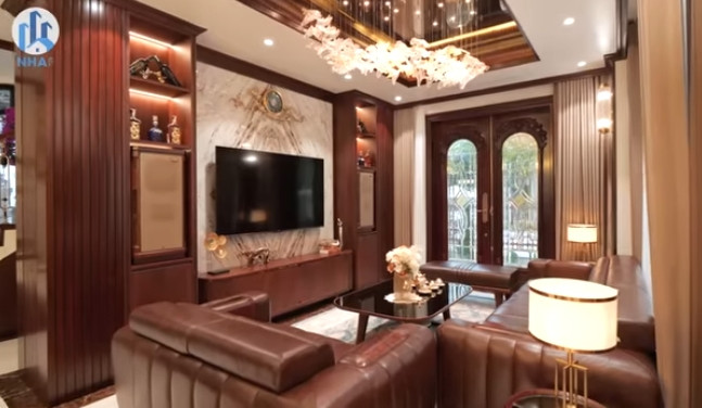 Phòng khách nổi bật với bộ sofa lớn. Xung quanh không gian phòng khách được sử dụng toàn bộ gỗ óc chó. Ảnh chụp màn hình NhaF