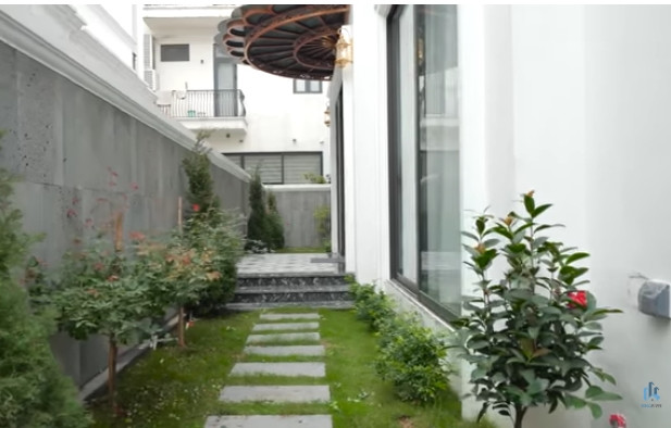 Bên hông nhà còn một lối đi trồng cây xanh và các loại hoa, dẫn tới một cửa kính lớn vào nhà. Ảnh chụp màn hình NhaF