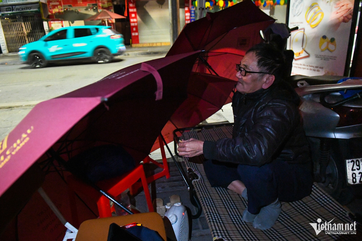 Ông Ngô Trọng Minh (bảo vệ) lúi húi dùng vài chiếc ô che chắn gió cho chiếc giường đặt trên vỉa hè phố Trần Nhân Tông. "Những ngày gần đây thường có mưa đêm, nhiệt độ hạ thấp nên rét buốt. Cứ vào mỗi ca trực đêm tôi lại che chắn như thế này để tránh gió rồi bật máy sưởi mini dưới chân để giữ ấm", ông Minh nói.