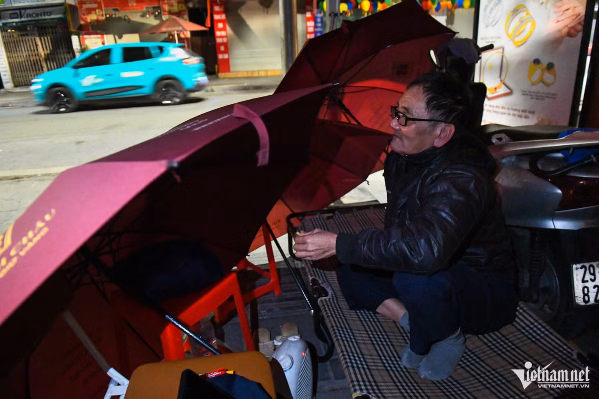 Ông Ngô Trọng Minh (bảo vệ) lúi húi dùng vài chiếc ô che chắn gió cho chiếc giường đặt trên vỉa hè phố Trần Nhân Tông. "Những ngày gần đây thường có mưa đêm, nhiệt độ hạ thấp nên rét buốt. Cứ vào mỗi ca trực đêm tôi lại che chắn như thế này để tránh gió rồi bật máy sưởi mini dưới chân để giữ ấm", ông Minh nói.