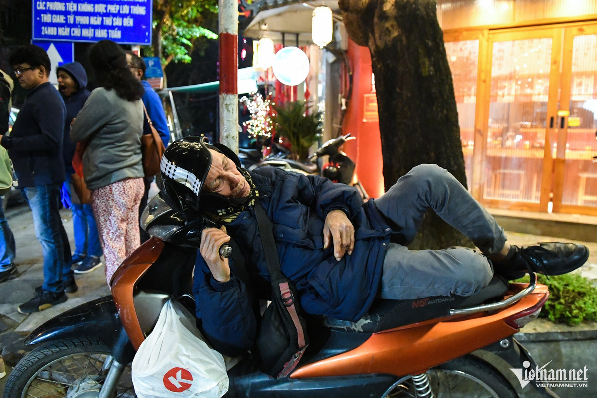 Đầu phố Lương Ngọc Quyến, một người lớn tuổi quàng khăn, đeo bịt tai, nằm lên yên xe máy trong bộ trang phục dày cộp.