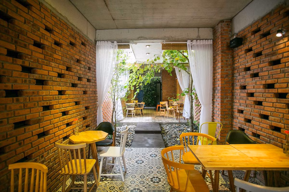 Tầng 1 là không gian kinh doanh cafe gồm quầy bar, bếp và khu vực pha chế. Khu vực này sử dụng cửa trượt gấp, nhiều cây xanh và ao cá để tạo không gian mở hoàn toàn. Ảnh: 85 Thiết kế