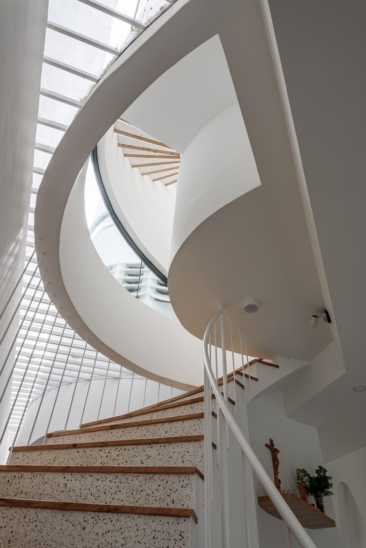 Cầu thang lên tầng theo khối cong của tòa nhà. Ý tưởng cắt khoét giếng trời mềm mại, giúp không gian sống luôn ngập ánh sáng tự nhiên. Ảnh: Lonton Studio