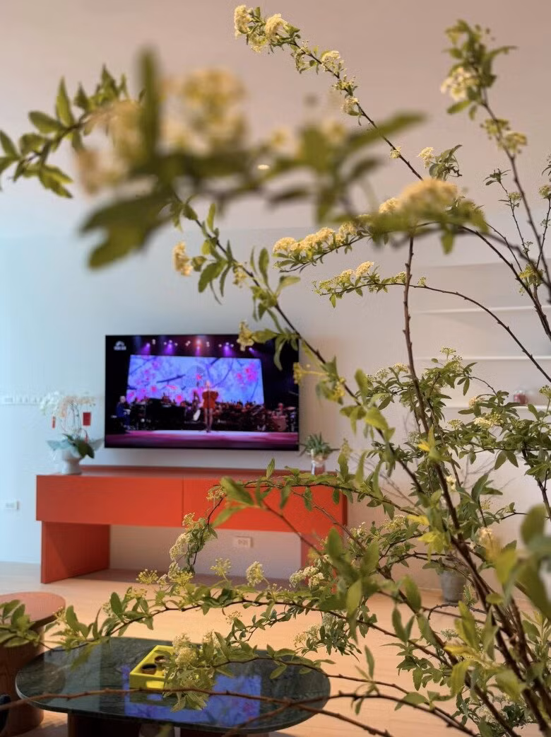 Phòng khách được tô điểm bởi những cành hoa trắng và chiếc kệ màu cam nổi bật. Ảnh: FBNV