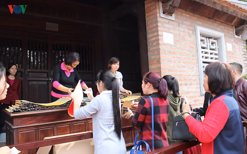 Hàng dài người xếp hàng mua giấy để xin chữ. Mỗi tờ giấy có giá 100.000 đồng. Mua giấy xong, mỗi người sẽ được phát một mã số đến bàn các ông đồ để xin chữ.