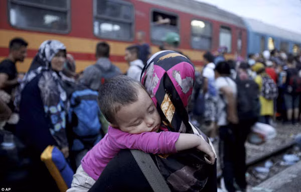 Một bà mẹ bồng đứa con đang ngủ hướng về đoàn tàu. Đa số người nhập cư đến từ các nước chìm trong chiến sự như Syria.