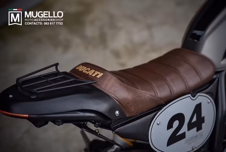 Tương tự, chiếc yên của xe cũng đã được khâu từ da bò. Đặc biệt, phần đuôi xe đã được độ lại hoàn toàn với khung phụ sửa đổi, yên solo kèm giá đèo hàng phía sau và đèn hậu LED tích hợp vào khung phụ. Nằm hai bên thân xe là các tấm ốp mới bằng nhôm được đánh số theo phong cách xe đua flat track.