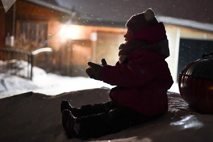 Nụ cười một bé gái mặc đồ rất ấm áp khi chơi đùa với tuyết.