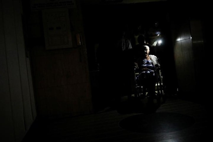 Người dân dùng ánh sáng từ điện thoại di động để giúp bà Olimpia Mora đi xe lăn ra khỏi một tòa nhà lúc bị cúp điện. Venezuela từng giàu có nhờ vào dầu mỏ nhưng giờ lại trong tình trạng thiếu điện nghiêm trọng.