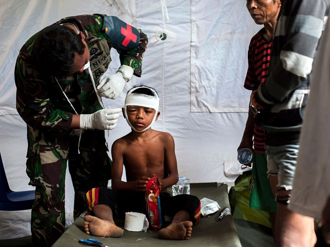 Nhân viên y tế trong quân đội đang băng vết thương trên đầu cho một cậu bé tại một bệnh viện ở Kayangan, đảo Lombok.