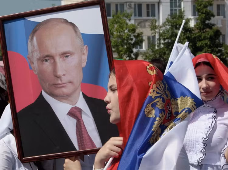 Một phụ nữ trẻ Chechnya mang theo một bức chân dung của Tổng thống Vladimir Putin trong một cuộc biểu tình kỷ niệm Ngày nước Nga ở Grozny, thủ đô Cộng hòa Chechnya.