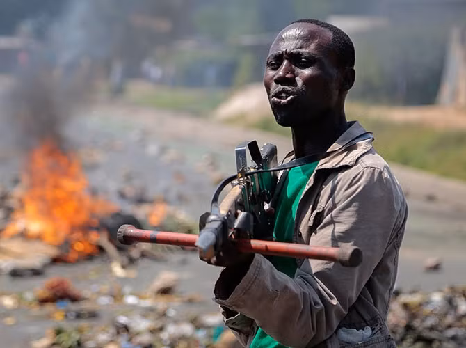 Một người biểu tình phản đối ở Thủ đô Bujumbura chĩa súng giả làm bằng gỗ về phía binh sĩ Burundi, trong một cuộc biểu tình phản đối Tổng thống Pierre Nkurunziza "tham quyền cố vị".