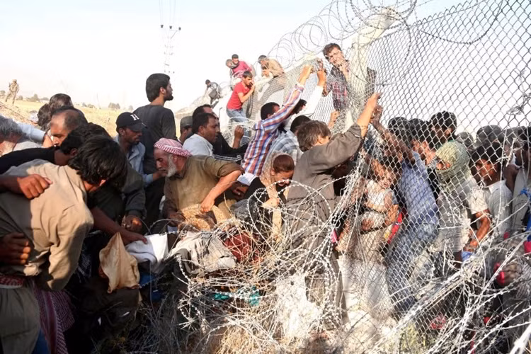 Hàng rào dây thép gai cũng không thể ngăn dòng người tị nạn. Trong ảnh: Hàng chục người tị nạn Syria xé rào chạy sang Akcale ở đông Nam Thổ Nhĩ Kỳ.