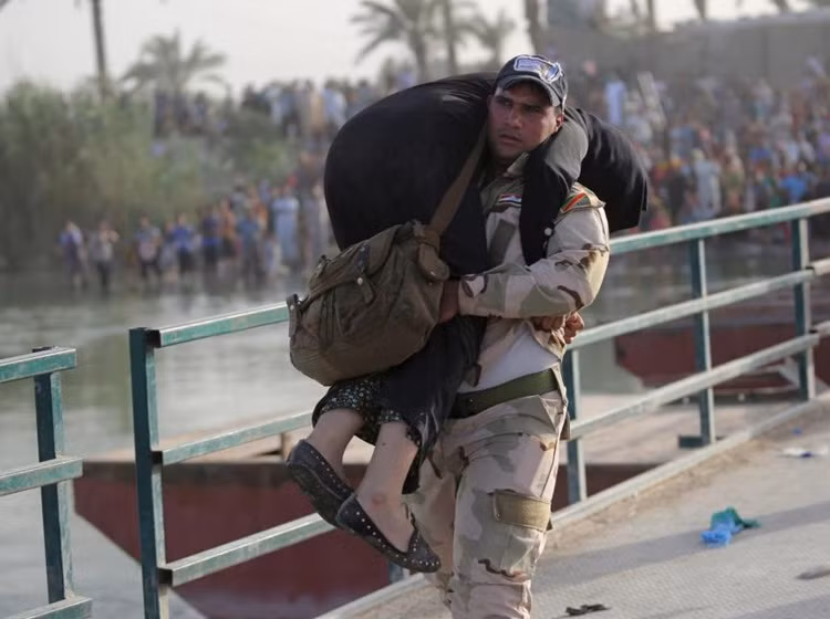 Binh sĩ Iraq bế một phụ nữ kiệt sức đi trên cầu.