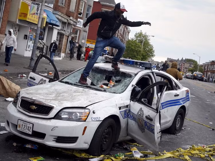 Sau khi tham dự đám tang Freddy Gray, đám đông đã tấn công cảnh sát, đốt phá các phương tiện giao thông và cửa hiệu, làm ít nhất 15 cảnh sát bị thương. Trong ảnh: Một thanh niên đập phá xe cảnh sát.