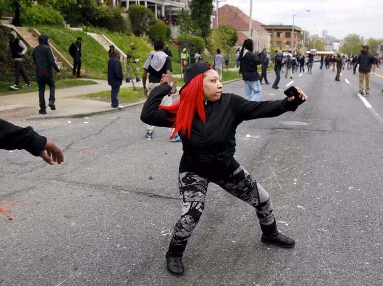 Một nữ thanh niên da màu ném đá vào cảnh sát.