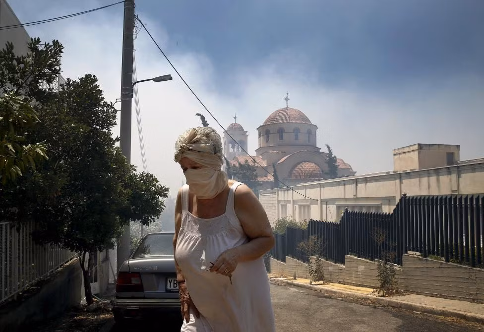 Người dân phải bịt kín mặt mũi để tránh khói bụi, khi ngọn lửa tiến gần Nhà thờ Saint George ở ngoại ô Athens ngày 17/7/2015.