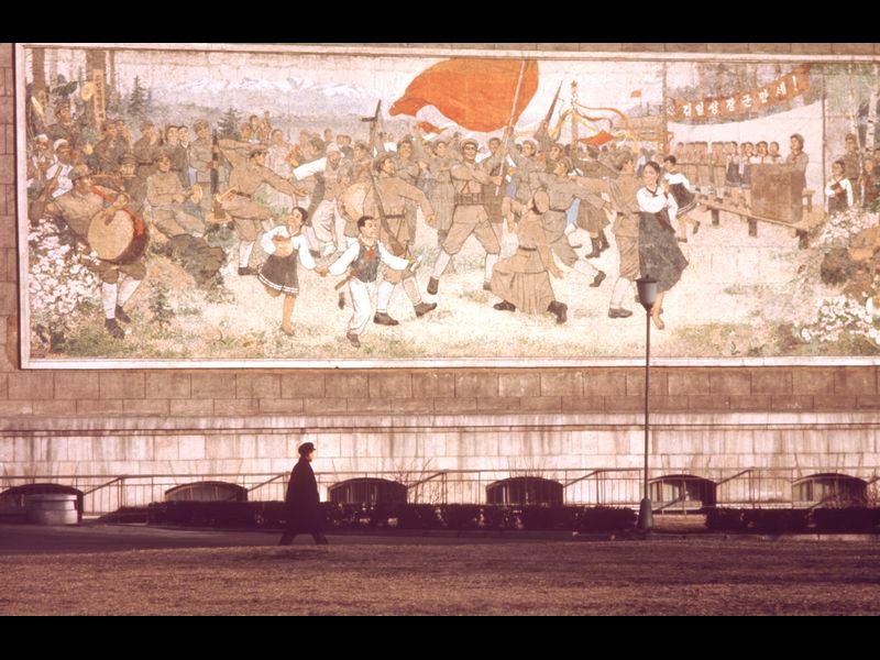 Một người đàn ông đi ngang qua bức tranh tường mô tả cuộc đấu tranh cách mạng của Triều Tiên.