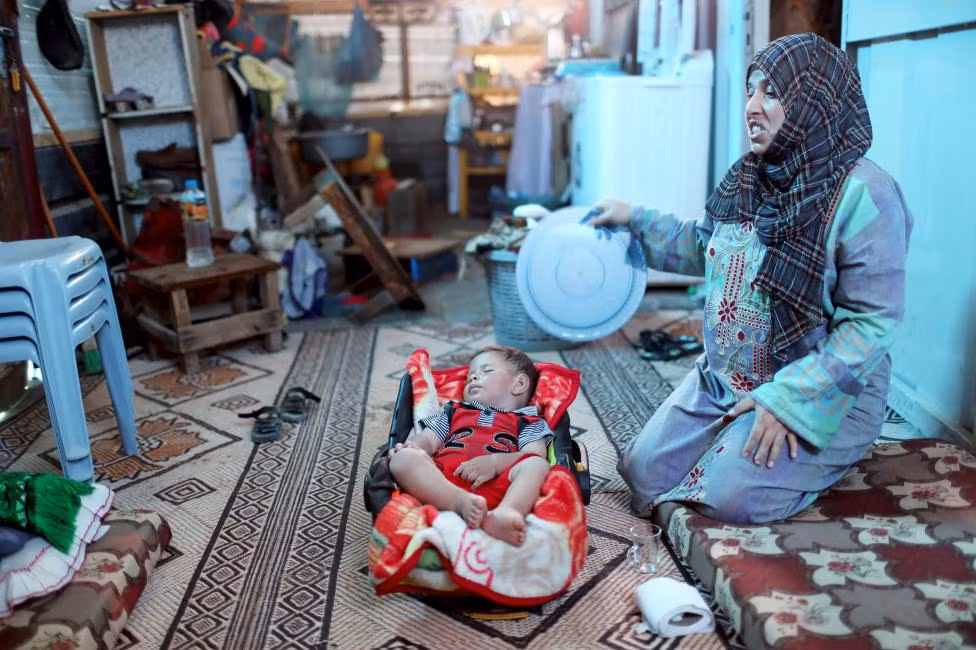 Người phụ nữ Palestine dùng chiếc khay để quạt mát cho con trong túp lều tạm bợ ở Khan Younis, phía nam Dải Gaza ngày 3/8.