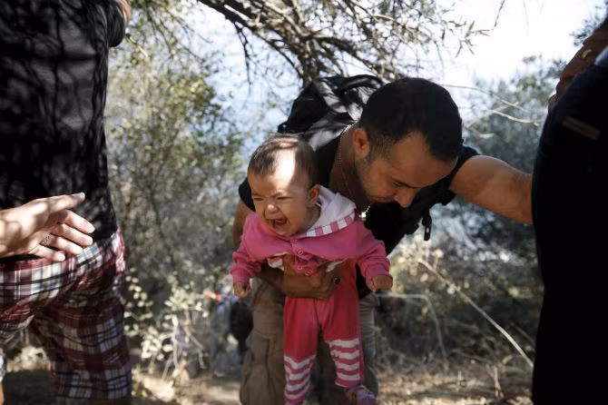 Một ông bố di dân người Afghanistan vừa bế con nhỏ trên tay vừa leo dốc sau khi họ tới đảo Lesbos, Hy Lạp, ngày 22/8/2015.
