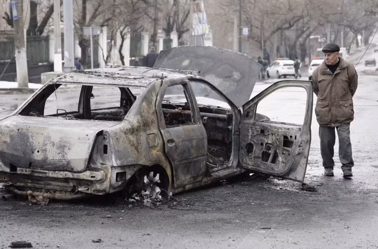 Người đàn ông quan sát chiếc xe ô tô bị cháy rụi gần bến dừng xe buýt ở Donetsk, Ukraine ngày 22/1/2015.