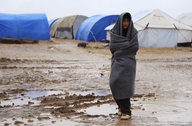 1 người tị nạn thuộc tộc người thiểu số Yazidi quấn 1 chiếc chăn đứng trên con đường trơn trượt ở trại tị nạn Nowruz ở thành phố Qamishli phía đông bắc Syria ngày 14/12/2014. 