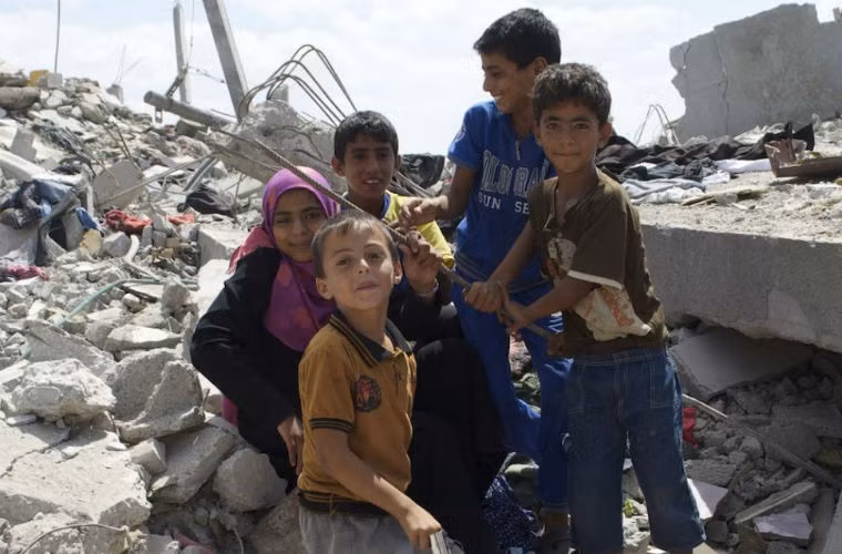 Thiếu nữ 15 tuổi cùng các em trai ngồi trên đống đổ nát đã từng là căn phòng của cô trước đây. Đống quần áo dưới chân cũng đã từng là tài sản của cô bé.