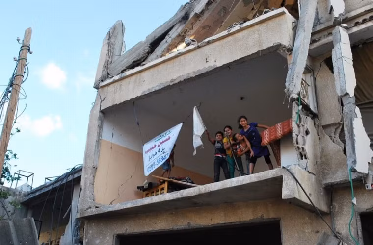 Lũ trẻ vui vẻ vẫy tay từ tầng thượng tòa nhà bị đạn pháo bắn phá. Mẹ chúng cho biết bà rất lo lắng ngôi nhà sẽ đổ sập vì đã hỏng hóc quá nhiều nhưng họ chẳng có nơi nào để đi.