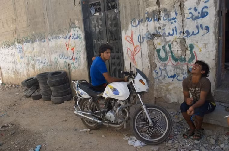 2 thanh niên ngồi bên ngoài ngôi nhà ở thành phố Beit Hanoun. Họ đang ở trong 1 trường học gần đó nhưng vẫn trở về ngôi nhà cũ thường xuyên để gặp gỡ gia đình và hàng xóm.