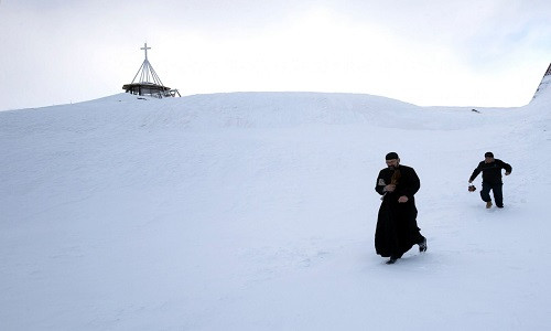 Linh mục cùng với trợ lý của mình đang bước đi trên tuyết gần nhà thờ được xây hoàn toàn bằng các tảng băng tuyết sau buổi lễ ban phước ngày 29/1