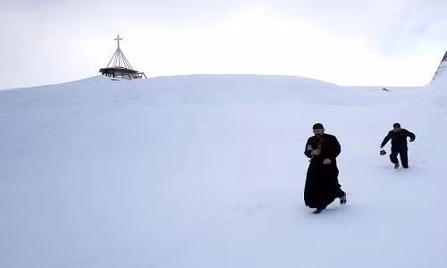 Linh mục cùng với trợ lý của mình đang bước đi trên tuyết gần nhà thờ được xây hoàn toàn bằng các tảng băng tuyết sau buổi lễ ban phước ngày 29/1