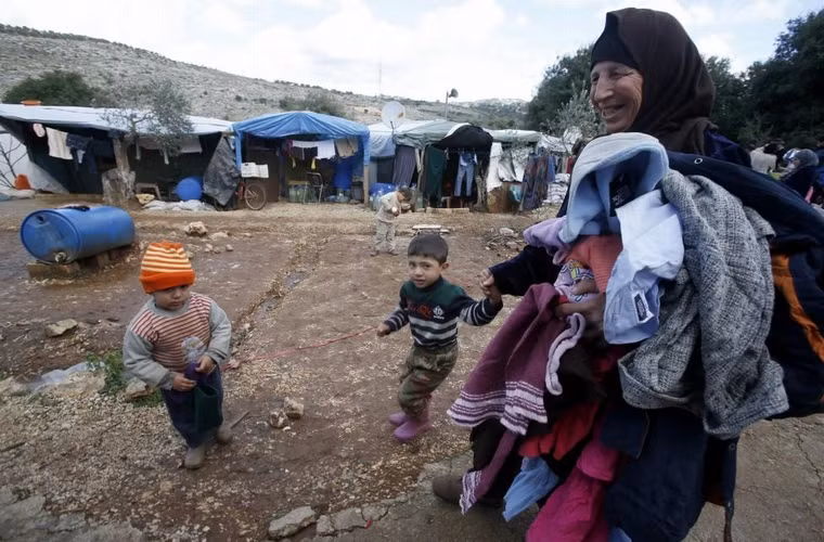 1 người phụ nữ tị nạn người Syria dắt tay 1 cậu bé sau khi nhận được quần áo ở khu vực định cư tạm thời ở làng Ketermaya, phía nam thủ đô Beirut, Lebanon ngày 8/1/2015. 