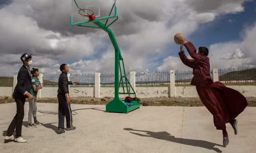 Một nhà sư đang chơi bóng rổ cùng bạn bè tại trường học trong cộng đồng tái định cư của Trung Quốc dành cho người dân du mục cũ.