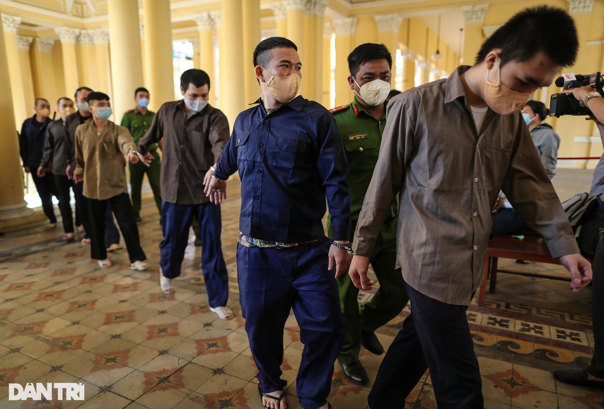 11 bị cáo khác cũng bị còng tay liền nhau và di chuyển vào bên trong phòng xét xử. Lực lượng công an siết chặt an ninh xung quanh.