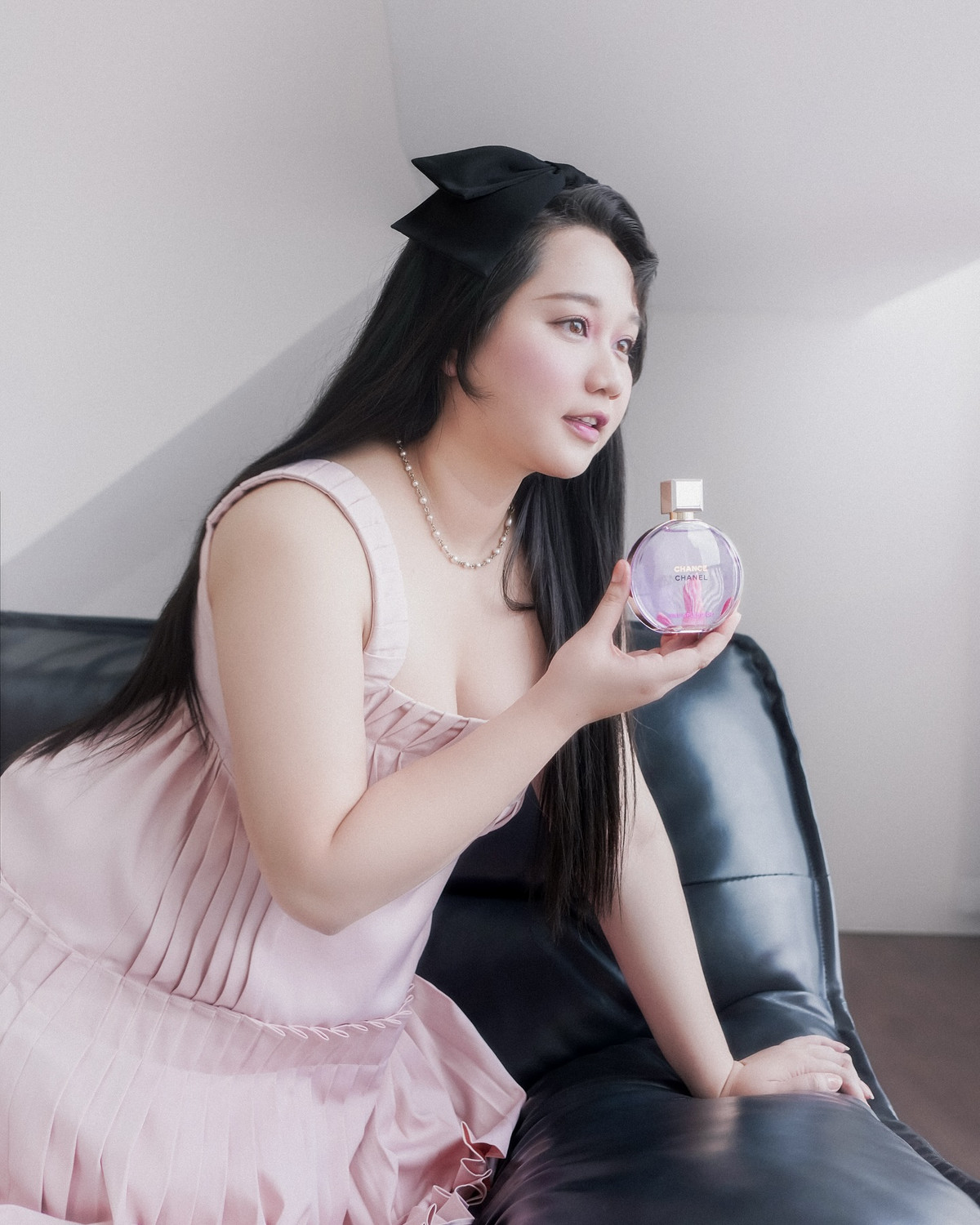 Điểm nhấn phụ kiện là chiếc nơ đen to bản trên mái tóc dài buông xoã, cùng chuỗi vòng cổ ngọc trai mang phong cách retro, tạo nên tổng thể hài hòa giữa sự trẻ trung và quý phái.