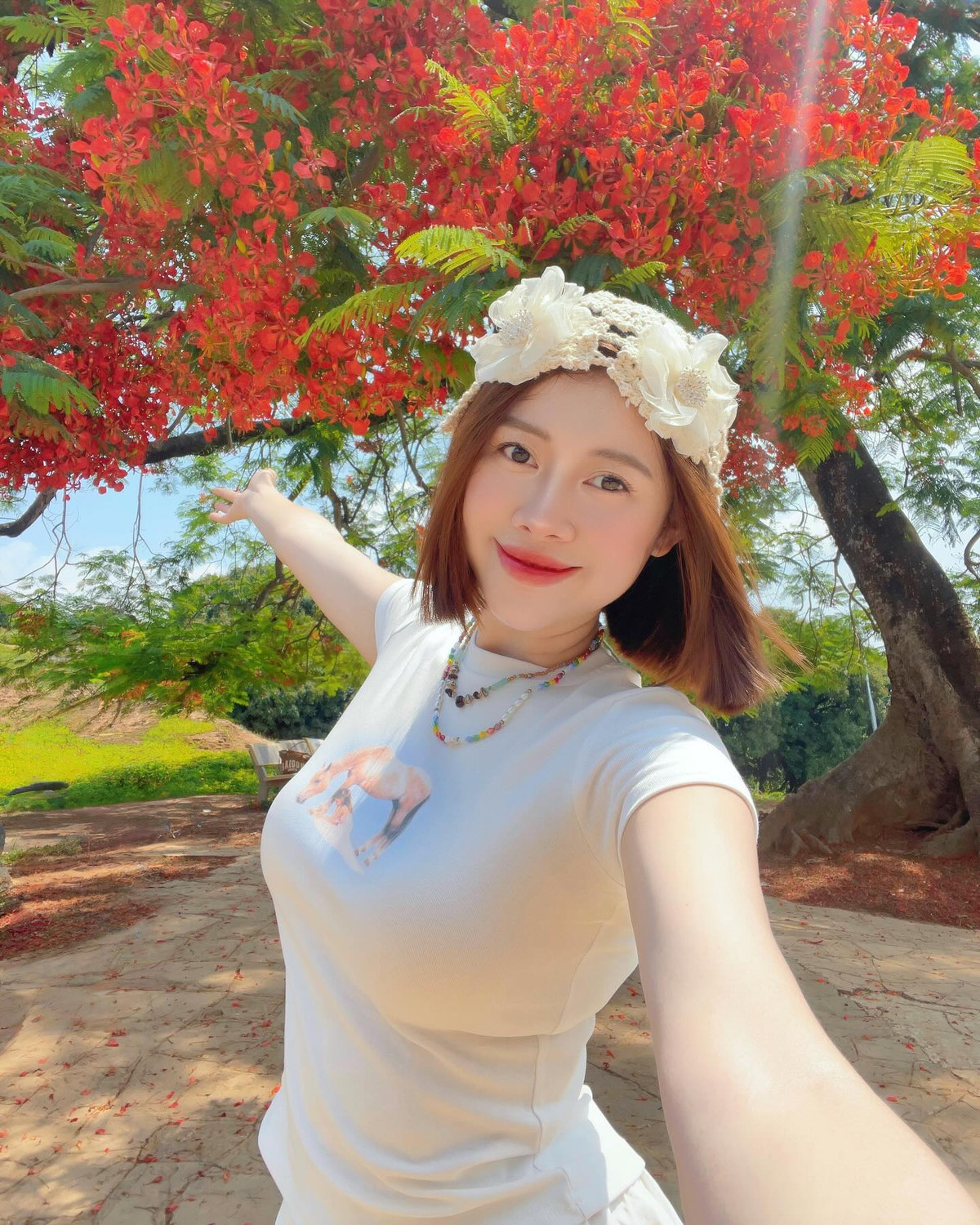 Giữa sắc đỏ rực rỡ của những chùm hoa phượng nở rộ trên nền trời xanh và không gian xanh mát của đồi A1, hình ảnh Việt Phương Thoa toát lên vẻ dịu dàng, thanh xuân và đầy nữ tính. Dưới nắng nhẹ, làn da trắng mịn cùng nụ cười tươi tắn của cô nàng khiến khung hình như được “thắp sáng”.