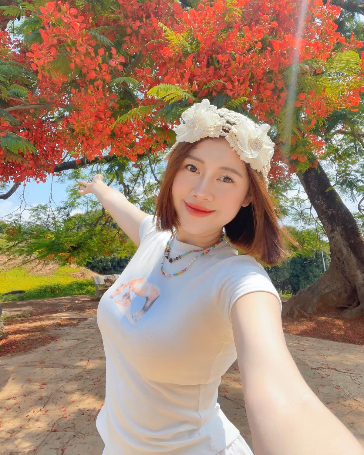 Giữa sắc đỏ rực rỡ của những chùm hoa phượng nở rộ trên nền trời xanh và không gian xanh mát của đồi A1, hình ảnh Việt Phương Thoa toát lên vẻ dịu dàng, thanh xuân và đầy nữ tính. Dưới nắng nhẹ, làn da trắng mịn cùng nụ cười tươi tắn của cô nàng khiến khung hình như được “thắp sáng”.