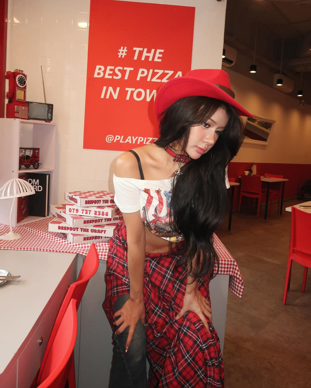 Phía dưới, cô nàng kết hợp với quần jeans bó sát và áo sơ mi caro đỏ buộc ngang hông – một chi tiết mang đậm hơi thở miền viễn Tây nước Mỹ, đồng thời tạo thêm điểm nhấn layer thú vị cho tổng thể set đồ.