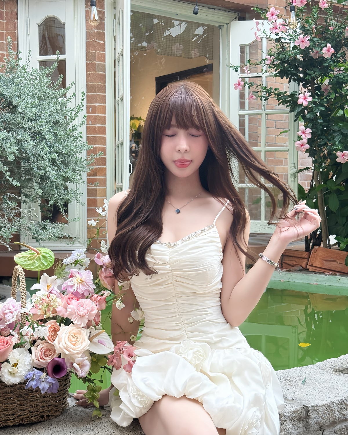 Diện váy trắng tinh khôi với thiết kế ôm nhẹ phần eo, nhấn nhá bằng những đường xếp nếp mềm mại và viền đá lấp lánh ở cổ áo, Tammy như hóa thân thành nàng thơ giữa khu vườn cổ tích.