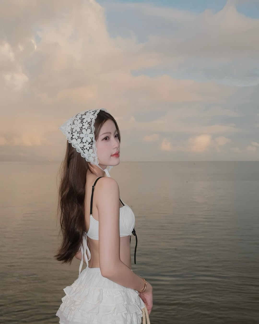 Màu trắng tinh khôi không chỉ tôn lên làn da trắng mịn mà còn mang lại cảm giác nhẹ nhàng, tinh khiết, rất phù hợp với không gian biển lúc bình minh.