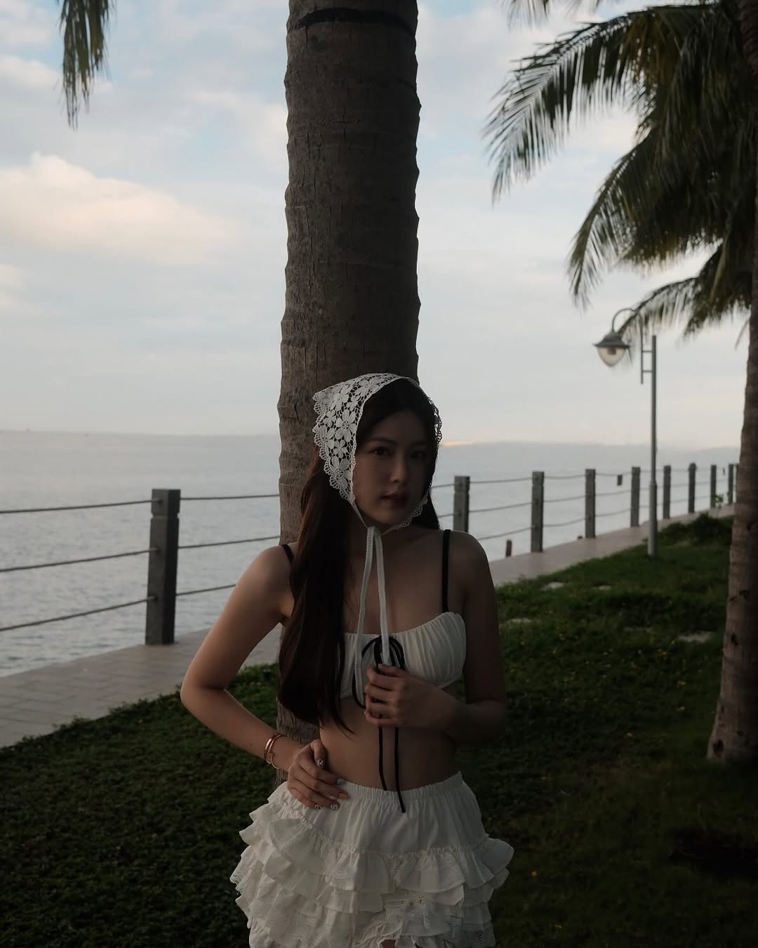 Chiếc mũ trùm đầu bằng ren trắng thắt nơ là phụ kiện tạo nên sự khác biệt. Phong cách vintage này đang trở lại mạnh mẽ và mang đến cho người mặc vẻ cổ điển, tiểu thư. Cùng với đó, chiếc túi cói cầm tay tăng thêm cảm giác mùa hè, hoàn thiện outfit theo phong cách "beach chic" một cách trọn vẹn.